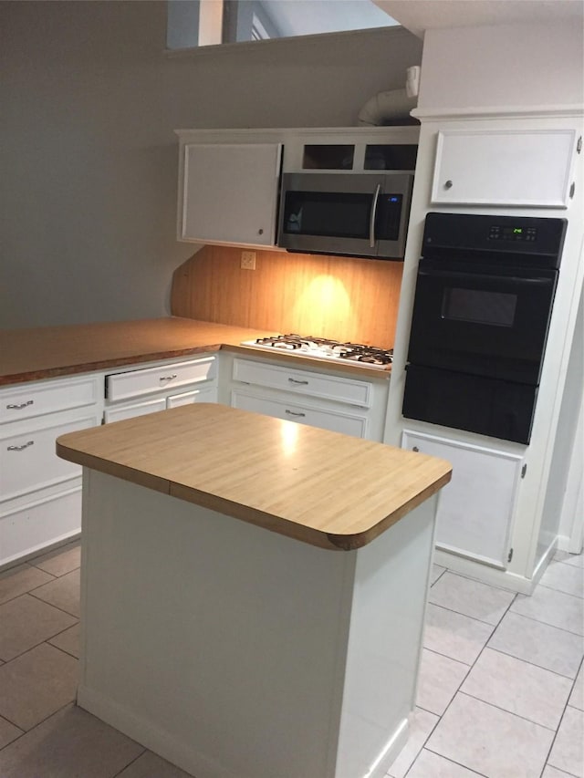 kitchen featuring light tile patterned flooring, oven, white gas stovetop, white cabinets, and stainless steel microwave