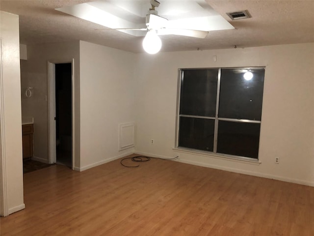 unfurnished room with a textured ceiling, wood finished floors, visible vents, baseboards, and a ceiling fan