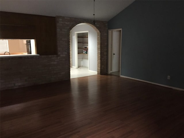 unfurnished room with lofted ceiling, arched walkways, and wood finished floors