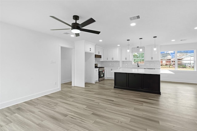 kitchen with white cabinetry, decorative light fixtures, stainless steel range with gas stovetop, a kitchen island, and backsplash