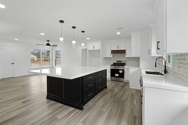 kitchen with pendant lighting, sink, white cabinetry, stainless steel range oven, and a kitchen island