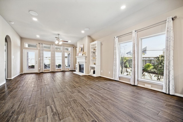 unfurnished living room featuring arched walkways, recessed lighting, dark wood-style flooring, baseboards, and a glass covered fireplace