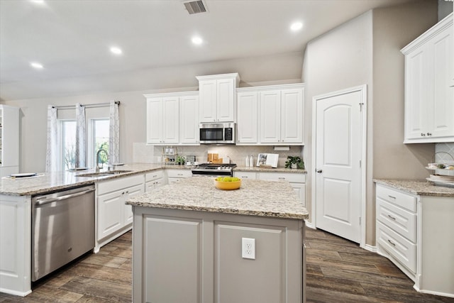 kitchen featuring stainless steel appliances, a peninsula, a sink, visible vents, and a center island