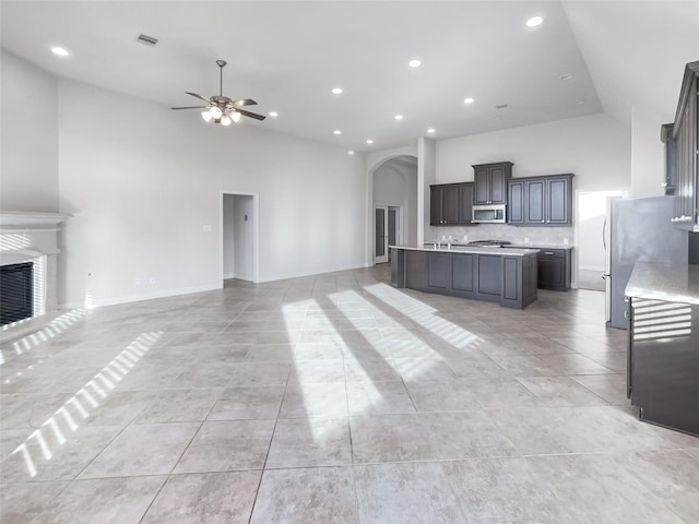 kitchen featuring high vaulted ceiling, appliances with stainless steel finishes, ceiling fan, a kitchen island with sink, and decorative backsplash