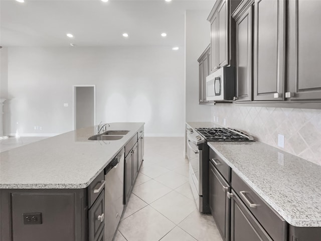 kitchen featuring sink, appliances with stainless steel finishes, an island with sink, light stone countertops, and backsplash