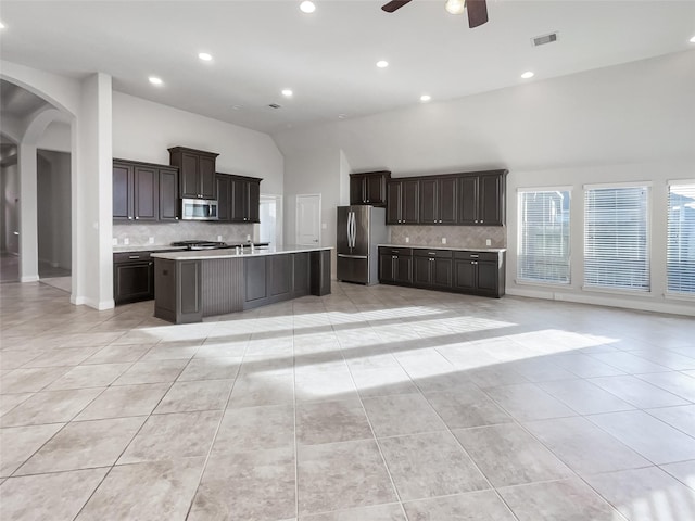 kitchen with light tile patterned flooring, high vaulted ceiling, ceiling fan, stainless steel appliances, and a center island with sink