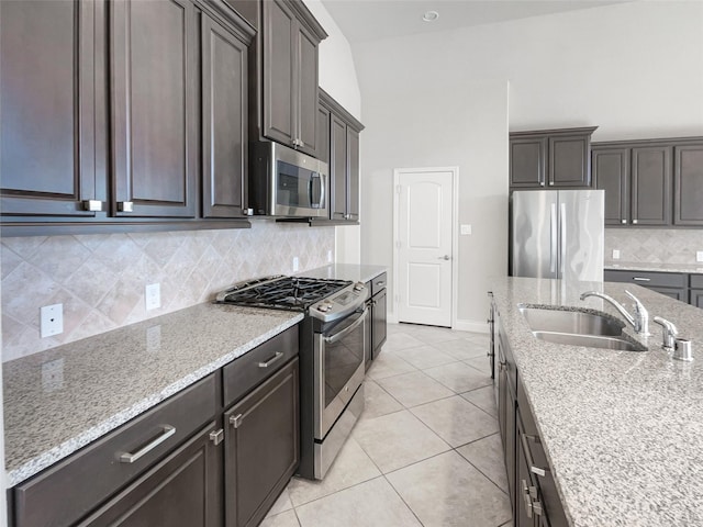 kitchen featuring stainless steel appliances, light stone countertops, sink, and light tile patterned floors