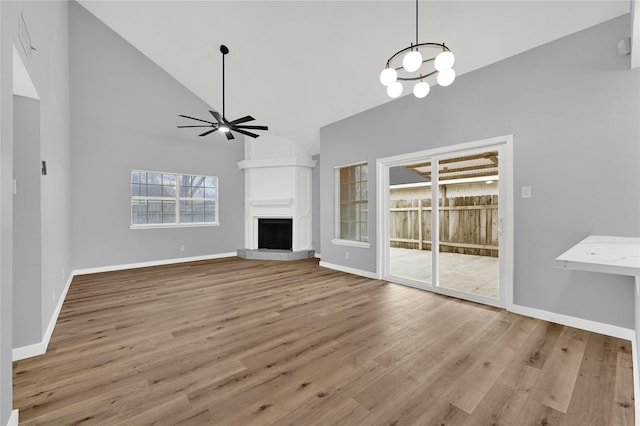 unfurnished living room with high vaulted ceiling, ceiling fan with notable chandelier, and light wood-type flooring