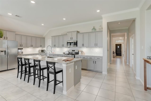 kitchen featuring gray cabinets, appliances with stainless steel finishes, an island with sink, sink, and light stone counters