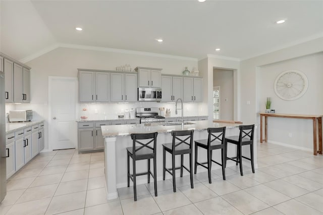 kitchen with appliances with stainless steel finishes, an island with sink, sink, gray cabinetry, and light stone counters