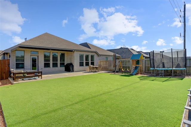 rear view of property featuring a playground, a lawn, a trampoline, and a patio area