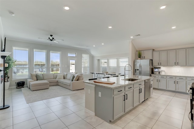 kitchen with appliances with stainless steel finishes, sink, light tile patterned floors, light stone counters, and a center island with sink