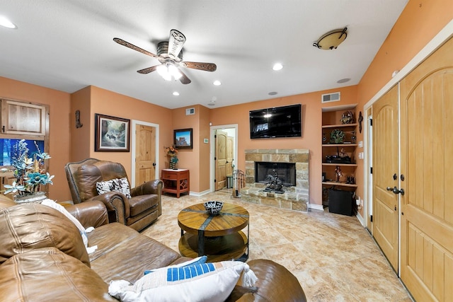 living room with built in shelves, ceiling fan, and a stone fireplace