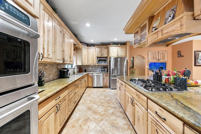 kitchen with stainless steel appliances, tasteful backsplash, light stone countertops, and light brown cabinets