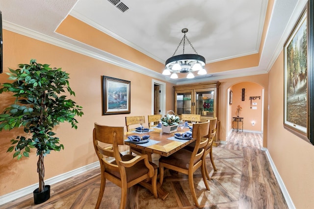 dining space with crown molding, a tray ceiling, and a chandelier