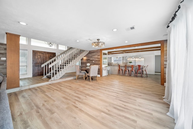 unfurnished living room featuring wood walls, an inviting chandelier, and light hardwood / wood-style floors