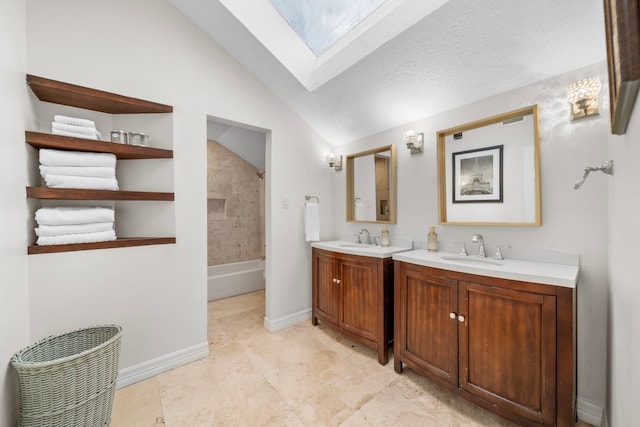 bathroom featuring vanity, vaulted ceiling with skylight, tiled shower / bath combo, and a textured ceiling