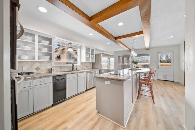 kitchen featuring light hardwood / wood-style flooring, stainless steel dishwasher, a kitchen island, beam ceiling, and light stone countertops