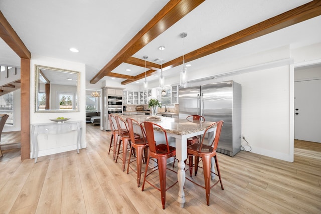 dining space with beam ceiling, sink, and light wood-type flooring