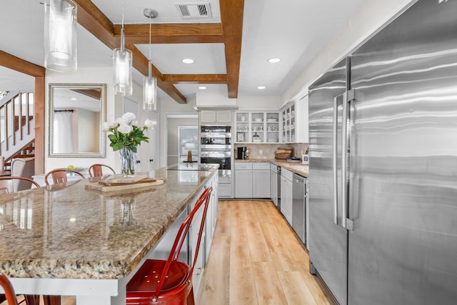 kitchen with decorative light fixtures, white cabinetry, a kitchen breakfast bar, stainless steel appliances, and light hardwood / wood-style flooring