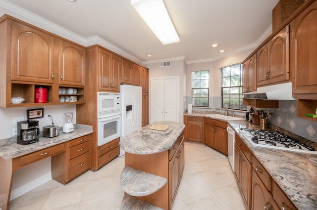 kitchen featuring sink, light stone counters, ornamental molding, a kitchen island, and white appliances