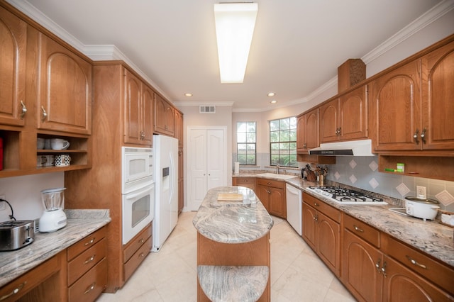 kitchen with sink, decorative backsplash, a center island, light stone countertops, and white appliances