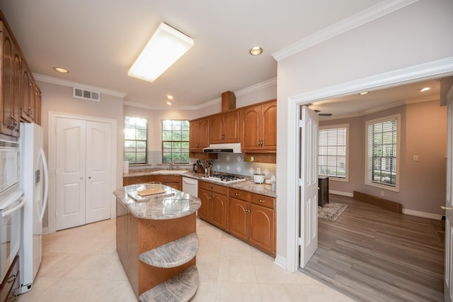 kitchen featuring white appliances, crown molding, light stone counters, a kitchen island, and decorative backsplash