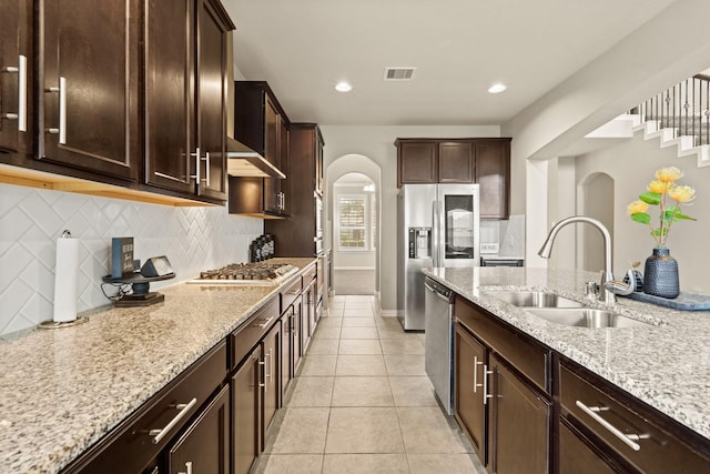 kitchen featuring sink, tasteful backsplash, dark brown cabinets, appliances with stainless steel finishes, and light stone countertops