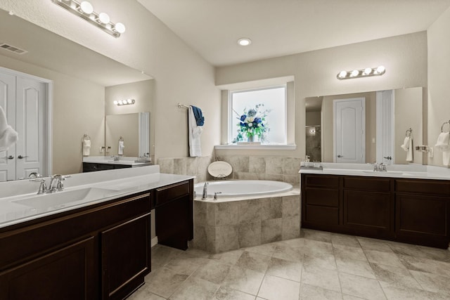 bathroom with a relaxing tiled tub, vanity, and tile patterned flooring