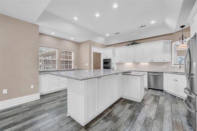 kitchen featuring light stone counters, hanging light fixtures, a kitchen island, stainless steel appliances, and white cabinets