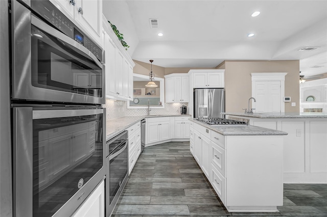 kitchen featuring pendant lighting, light stone counters, white cabinets, and appliances with stainless steel finishes