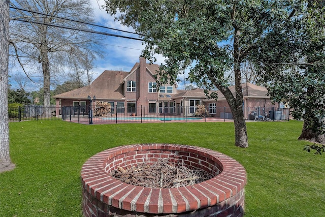 rear view of property with a fenced in pool, a yard, and a fire pit