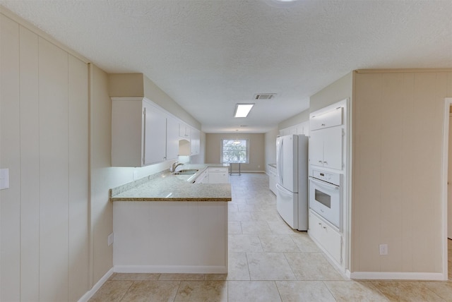 kitchen with sink, white appliances, a textured ceiling, white cabinets, and kitchen peninsula