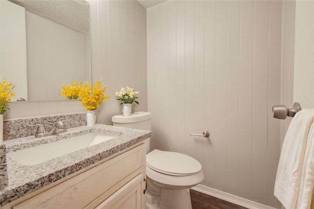 bathroom with vanity, wood-type flooring, wood walls, and toilet