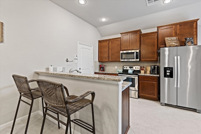 kitchen featuring light stone countertops, stainless steel appliances, kitchen peninsula, and a breakfast bar