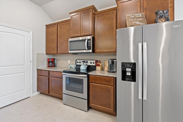 kitchen with lofted ceiling, decorative backsplash, light tile patterned floors, stainless steel appliances, and light stone countertops