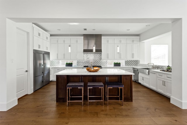 kitchen featuring dark wood-type flooring, white cabinetry, stainless steel appliances, a kitchen island, and wall chimney exhaust hood