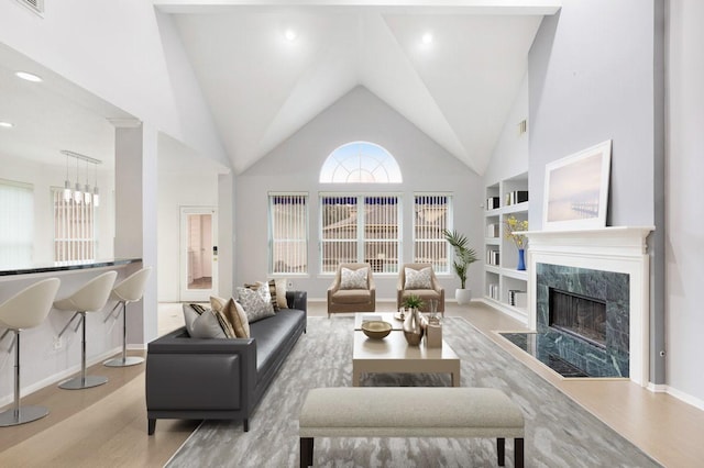 living room featuring high vaulted ceiling, light hardwood / wood-style flooring, built in features, a notable chandelier, and a premium fireplace