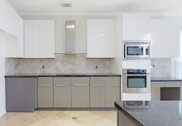 kitchen with appliances with stainless steel finishes, decorative backsplash, dark stone counters, ornamental molding, and wall chimney range hood