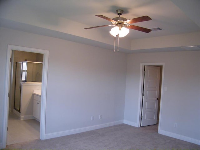 spare room with ceiling fan, a tray ceiling, and light carpet