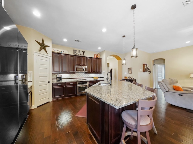 kitchen with appliances with stainless steel finishes, pendant lighting, sink, a kitchen bar, and a kitchen island with sink