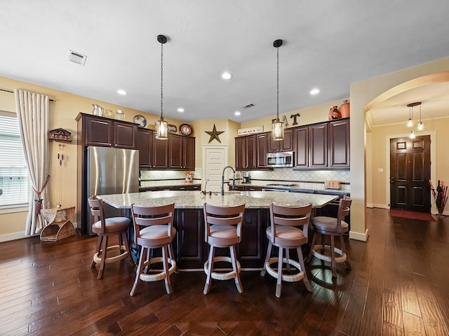 kitchen featuring appliances with stainless steel finishes, dark hardwood / wood-style floors, hanging light fixtures, and a large island with sink