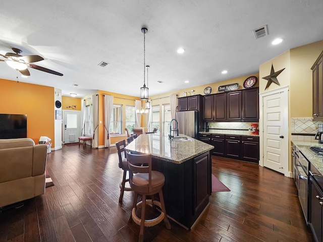 kitchen featuring hanging light fixtures, a kitchen island with sink, dark wood-type flooring, and dark brown cabinetry