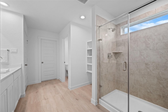 bathroom featuring hardwood / wood-style flooring, walk in shower, vanity, and toilet