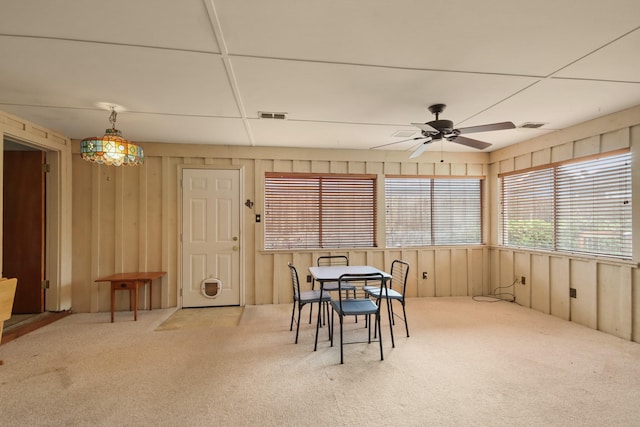 carpeted dining room featuring ceiling fan and wood walls