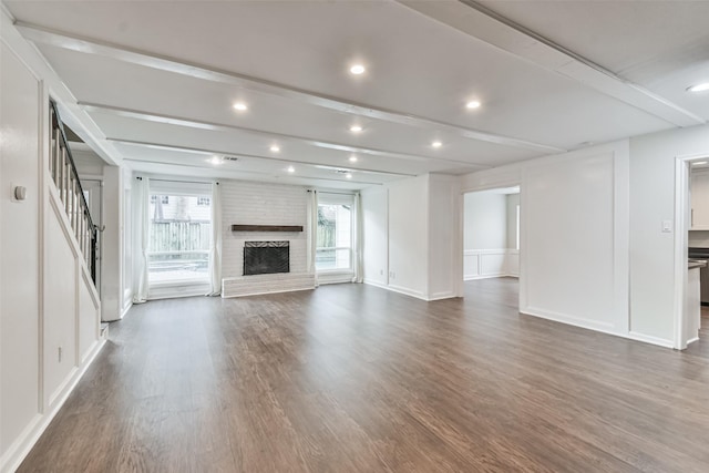 unfurnished living room with a fireplace, beam ceiling, and dark wood-type flooring