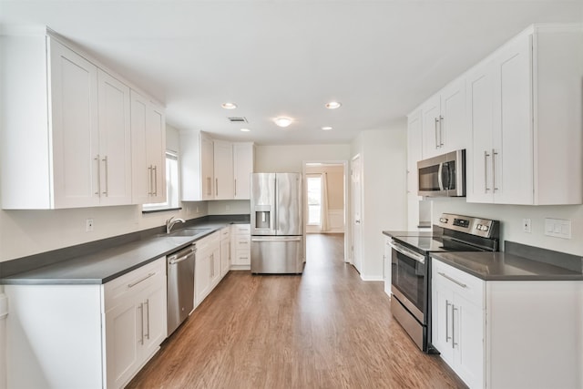 kitchen with stainless steel appliances, white cabinetry, wood-type flooring, and sink