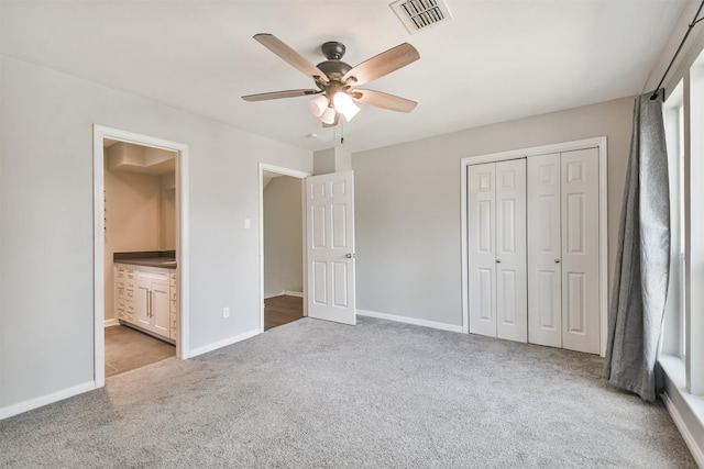 unfurnished bedroom with ceiling fan, a closet, ensuite bath, and light carpet