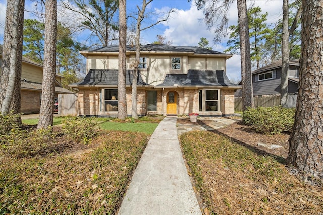 view of front of home with roof with shingles, brick siding, fence, and stucco siding