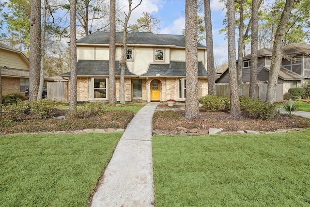 view of front facade featuring brick siding, fence, a front lawn, and stucco siding